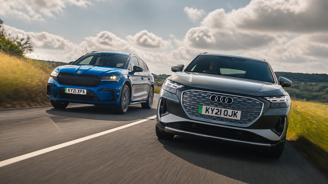 Zwei Elektro-SUVs, ein grauer Audi und ein blauer Skoda, fahren auf einer Landstraße bei bewölktem Himmel.