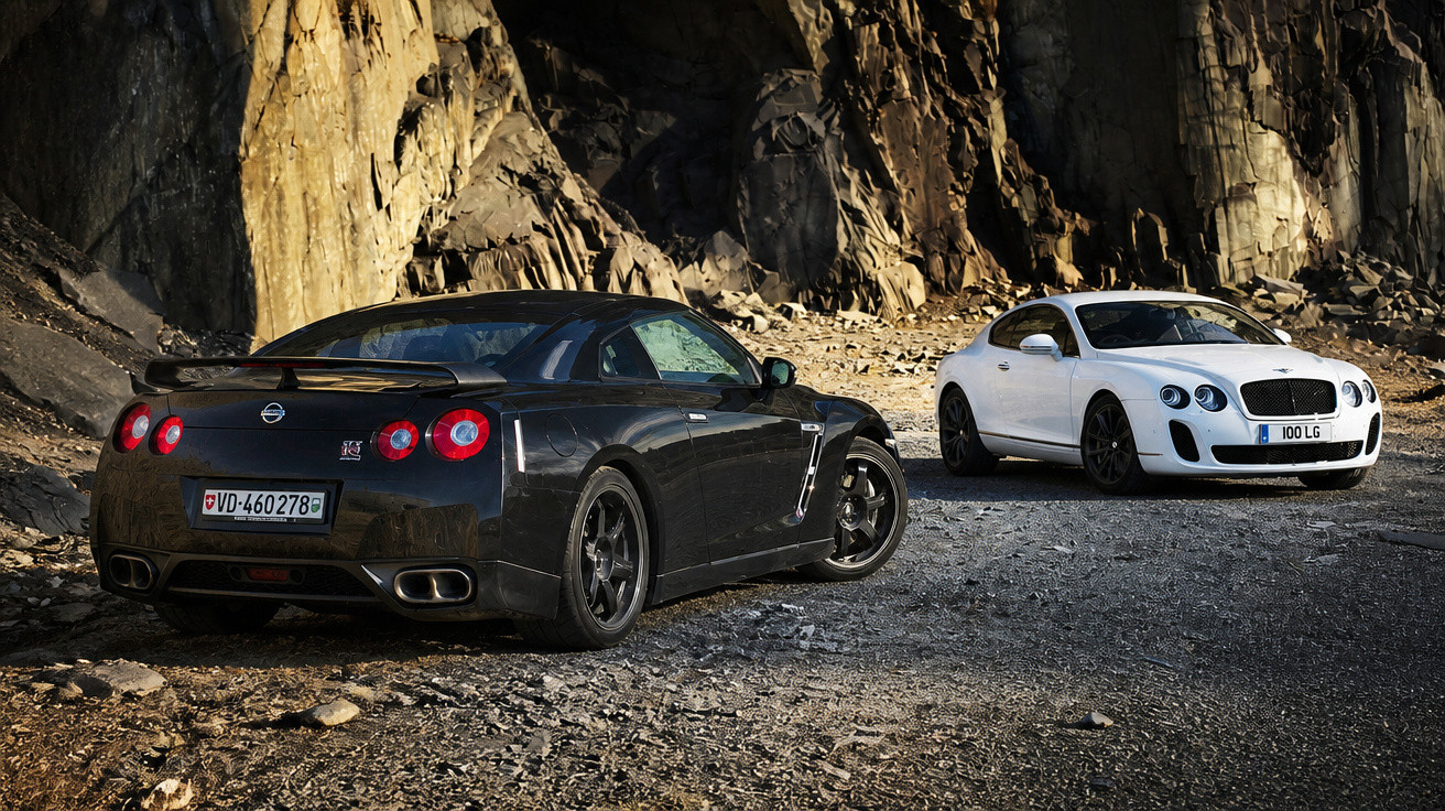 Schwarzer Nissan GT-R und weißer Bentley Continental GT auf felsigem Gelände vor Felswand.