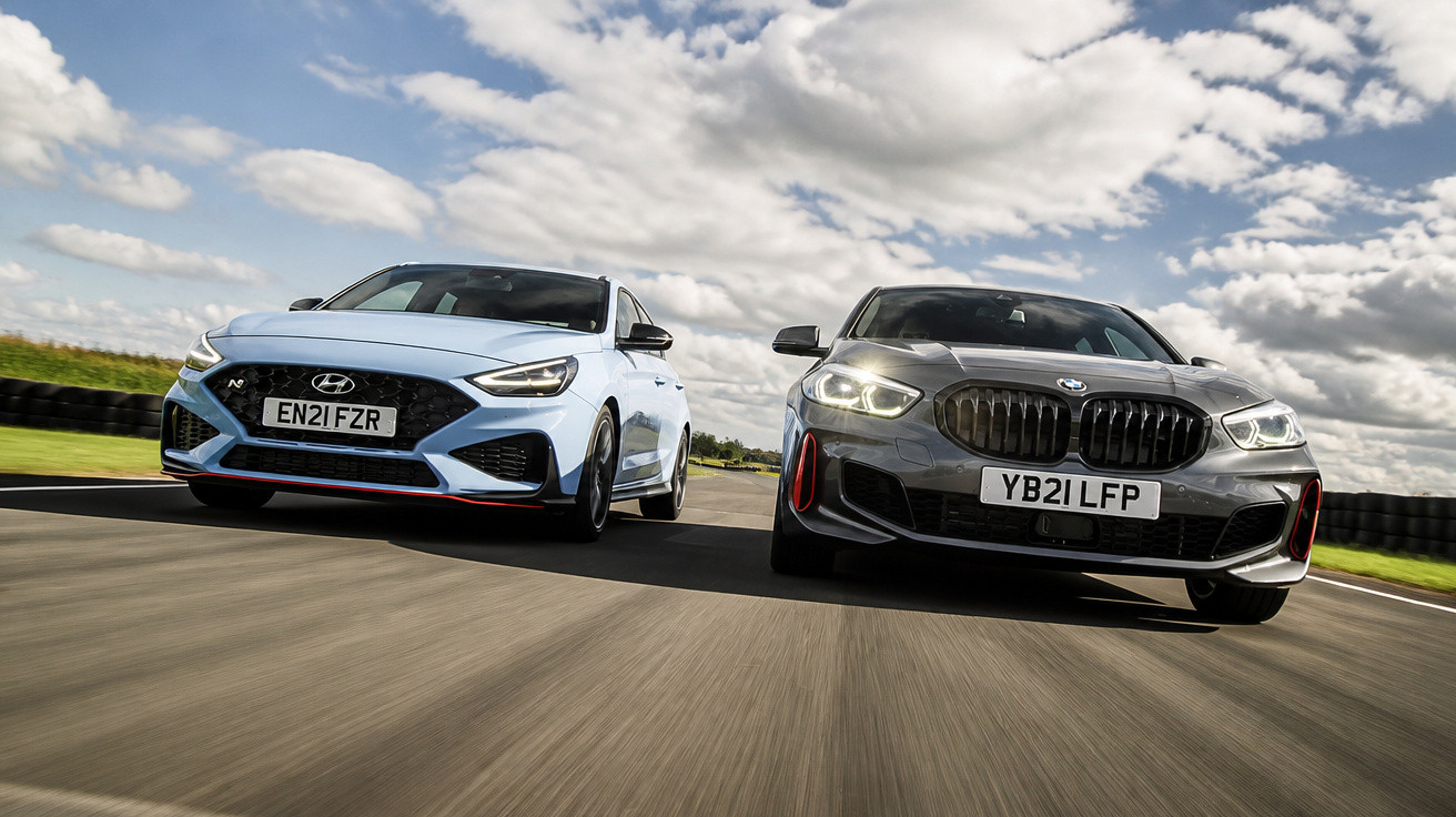 Zwei sportliche Autos, ein weißer Hyundai und ein grauer BMW, fahren nebeneinander auf einer Rennstrecke bei bewölktem Himmel