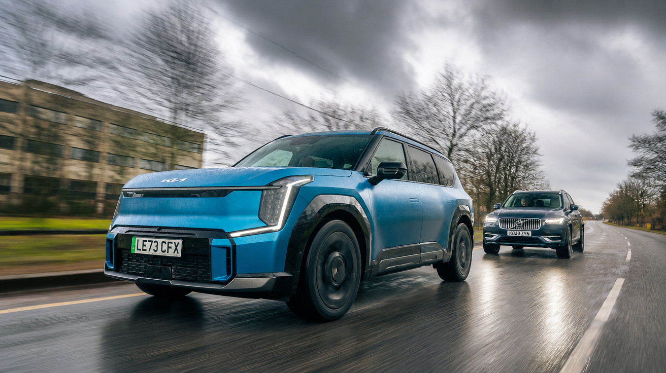Blauer Kia EV9 SUV fährt auf nasser Straße mit grauem Volvo SUV im Hintergrund unter bewölktem Himmel.