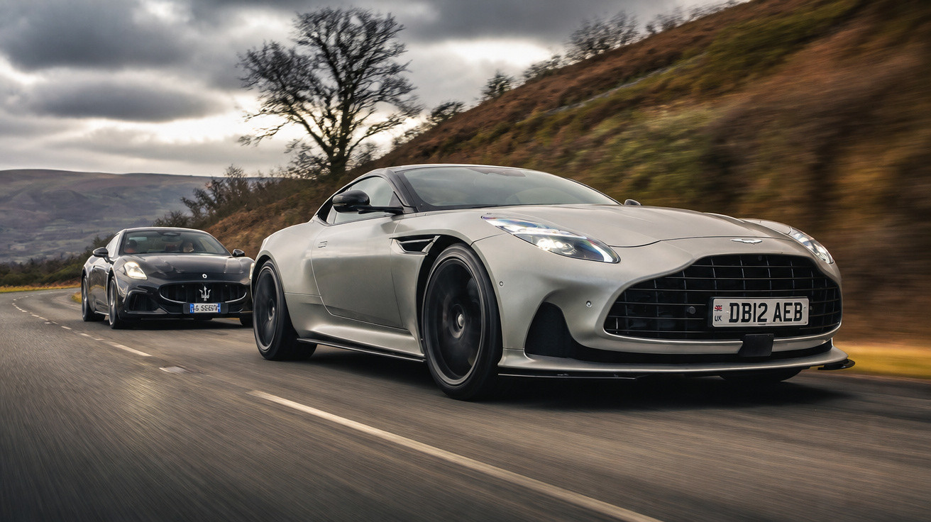 Zwei Sportwagen fahren auf einer kurvigen Landstraße bei bewölktem Himmel, vorne silberner Aston Martin.