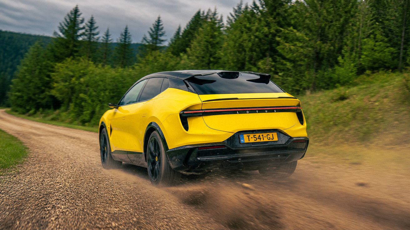 Gelber Lotus SUV fährt auf staubiger Schotterstraße umgeben von grünen Bäumen und bewölktem Himmel