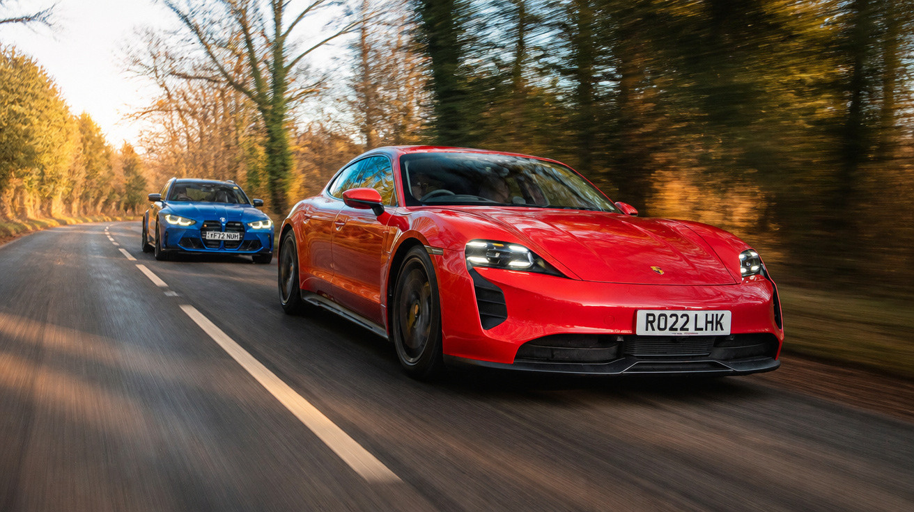 Roter Porsche fährt vorne, blauer BMW folgt auf herbstlich bewaldeter Landstraße bei Sonnenlicht.