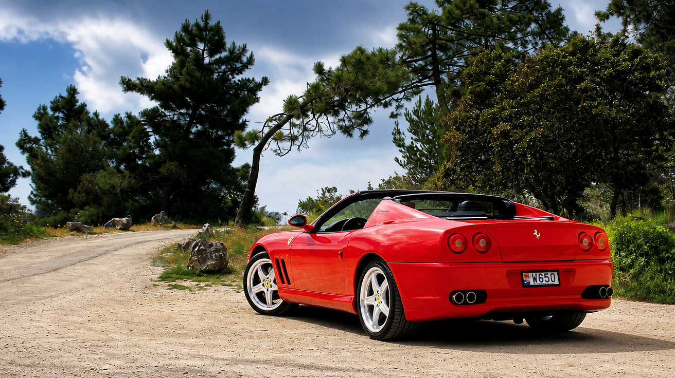 Roter Ferrari Sportwagen auf unbefestigter Straße mit Bäumen und bewölktem Himmel im Hintergrund.