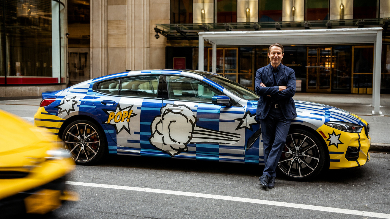 Mann lehnt an bunt lackiertem Auto mit Comic-POP-Motiv in urbaner Straße vor Gebäude.