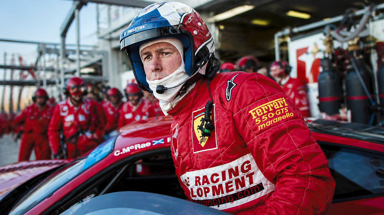 Mann im roten Ferrari-Racing-Anzug und Helm steigt aus Rennwagen, Teammitglieder im Hintergrund in Garage.