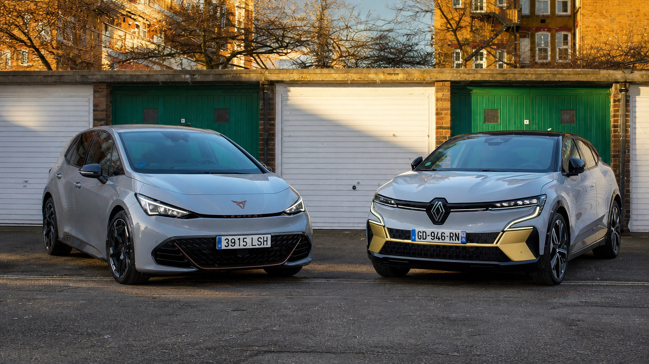 Zwei moderne weiße Elektroautos stehen vor einer Hauszeile mit weißen und grünen Garagentoren bei Sonnenlicht.